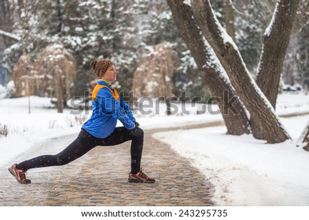 Young woman doing stretching exercises during winter training outside in cold snow weather in park