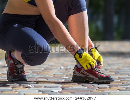 Sport woman model tying running shoes during training outside