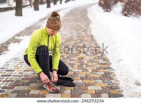 Young sport woman  tying running shoes during winter training outside in cold snow weather in park