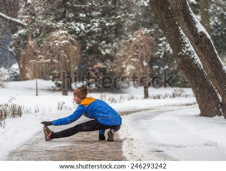 Young sport woman  stretching during training outside in cold snow weather in park