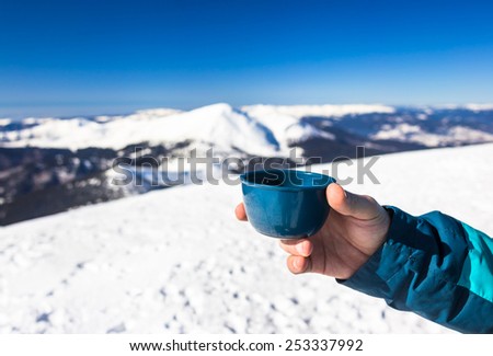 Happy man holding hot cup thermos on mountain top in winter