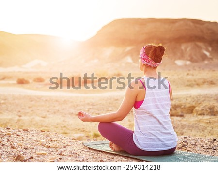 Young woman doing yoga in desert at sunrise time