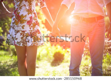 Young couple in love holding hands in the sunset in summer evening. Bright toning picture