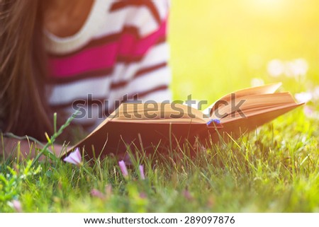 Young woman reading book in city park at summer day