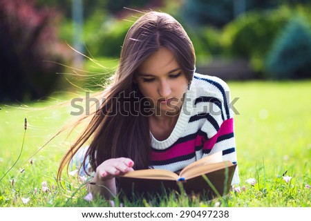 Young pretty woman reading book in city park at summer day