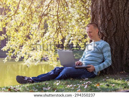 Young man with laptop sitting in green park. Student study in city park.