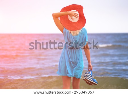Young woman in red hat walking on beach in the sea in sunny hot day