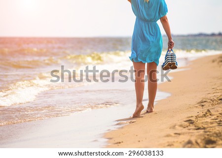 Young woman with sandals walking on beach in the sea in sunny hot day