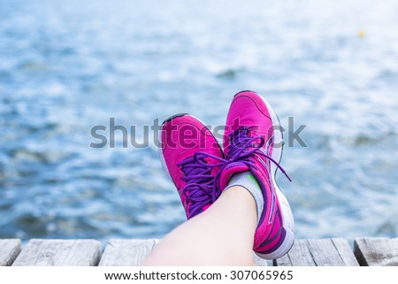 Sport woman's legs with pink sneakers relax on wooden pier near sea