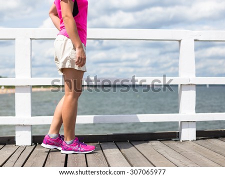 Sport woman with pink sneakers relax on wooden pier near sea