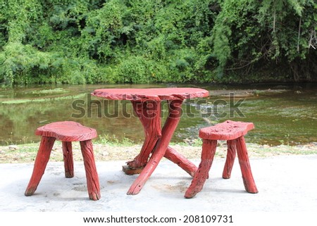 set of handmade red table and chairs outdoor next to the calm lake and green bush on a beautiful sunny day