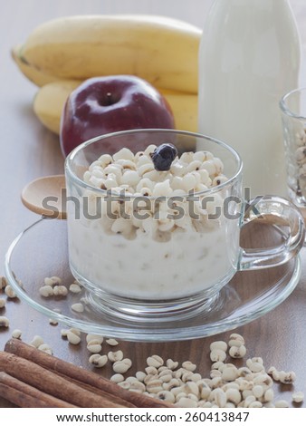 cooked Job\'s tear in sweet coconut milk in glass cup with dry Job\'s tear, cinnamon, star anise ,bottle of milk, apple and banana on wood table