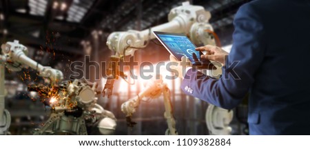 Manager industrial engineer using tablet check and control automation robot arms machine in intelligent factory. Welding robotics and digital manufacturing operation. Industry 4.0 concept