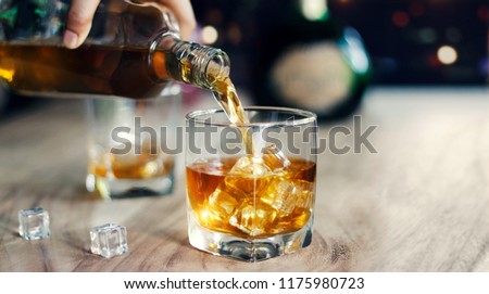 Man pouring whiskey in glasses of whisky drink alcoholic beverage with friends at bar counter in the pub.