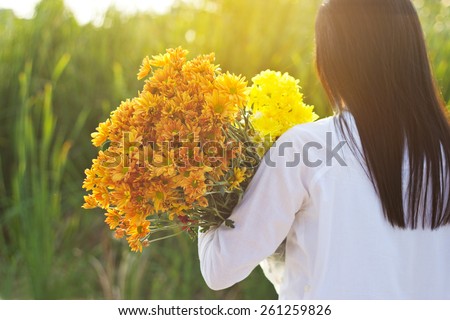 abstract woman with bouquet flowers vibrant in hands on grass field sunset background, warm tone, soft focus and blur