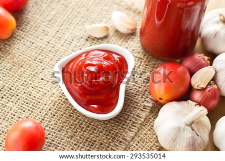 ketchup in bowl heart shape on sack and wooden background, warm color tone