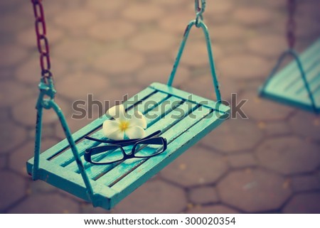 vintage color tone style, glasses and white flower on the blue swing in evening, soft focus