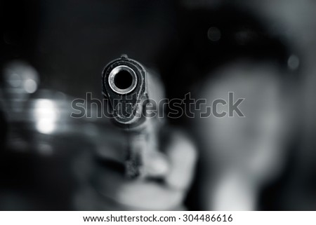 Black and white, woman pointing a old gun to front with one Hand on dark background