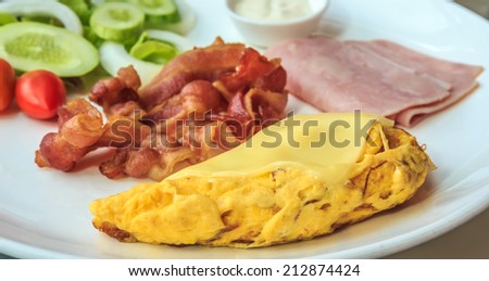 Omelet on top with cheese, bacon, ham, and salad