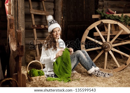 Smiling young woman in the village barn with knitting in hand