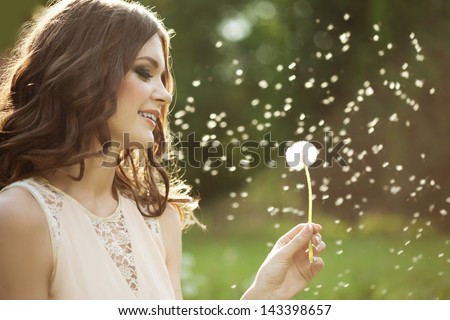 Beautiful young woman blowing a dandelion