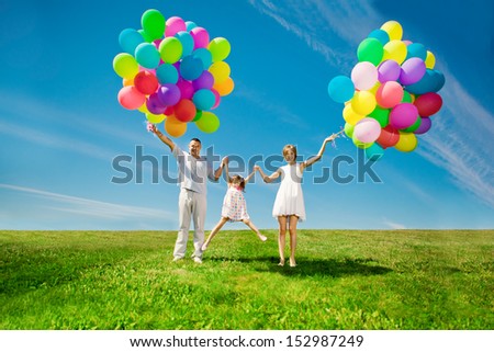 Happy family holding colorful balloons outdoor. Mom, dad and two daughters playing on  a green meadow.