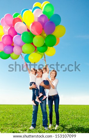 Happy family holding colorful balloons outdoor. Mom, dad and two daughters playing on  a green meadow.