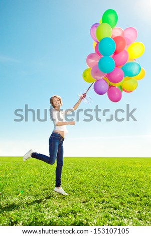 Beauty woman with balloons in hands in the field against the sky in the green garden.