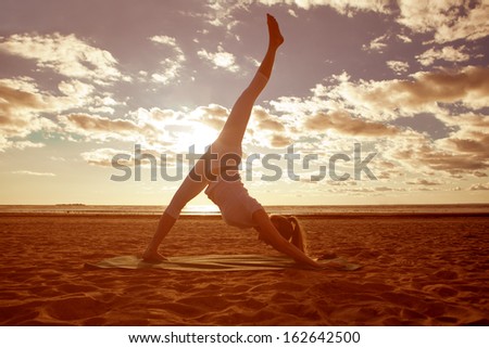 Young beautiful slim woman silhouette practices yoga on the beach at sunrise. Yoga at  sunset