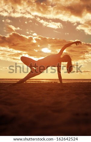 Young beautiful slim woman silhouette practices yoga on the beach at sunrise. Yoga at  sunset