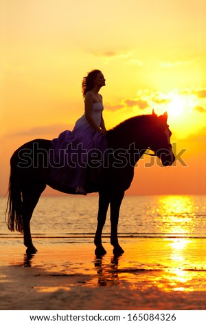 Beautiful Woman Riding A Horse At Sunset On The Beach. Young Beauty Girl With A Horse In The Rays Of The Sun By The Sea.
