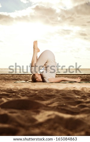 Young beautiful slim woman practices yoga on the beach at sunset. Yoga at sunrise