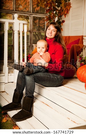 Beautiful woman with a child on the front porch with pumpkins autumn. Smiling mother and son.