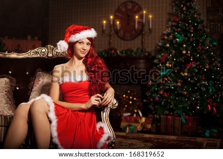 Young beautiful smiling santa woman near the Christmas tree. Fashionable luxury  girl celebrating New Year.