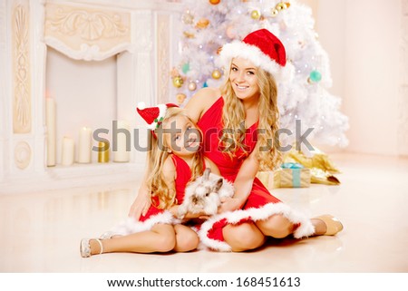 Mom and daughter dressed as Santa celebrate Christmas. Family at the Christmas tree. Woman and girl celebrate new year with bunny