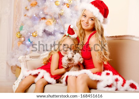 Mother and daughter dressed as Santa celebrate Christmas. Family at the Christmas tree. Woman and girl celebrate new year with bunny