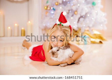 Beauty little Santa girl near the Christmas tree.  Happy girl with bunny celebrates  christmas.