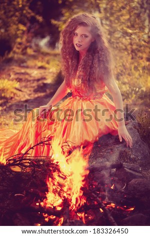 Beautiful witch in the woods near the fire. Magic woman celebrating Halloween. Girl doing witchcraft in the forest.