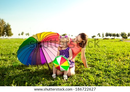 Beautiful little girl with mother rainbow umbrella holding  in  the park. Smiling child and mom on a field with flowers. Kid with mum rest on the  nature. Family outdoor