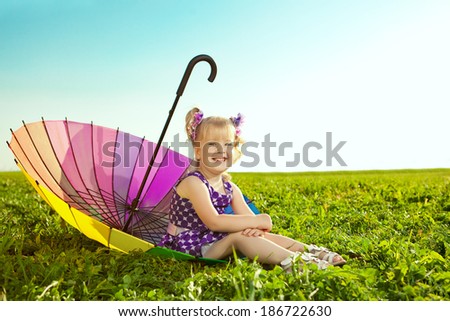 Cute little girl with rainbow umbrella on the grass in the park. Smiling nice child on  a field with flowers. Kid rest on the nature. Portrait of baby outdoor