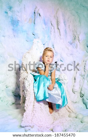 Little girl in princess dress on a background of a winter fairy tale. Baby snow queen. Sweet smiling child snowy kingdom. Kid in in carnival costume.