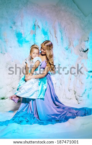Little girl with mother in princess dress on a background of a winter fairy tale. Baby and mom snow queen. Smiling child and mum snowy kingdom. Kid in in carnival costume.
