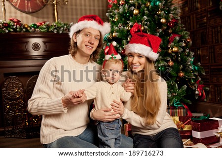 Happy smiling young family near the Christmas tree celebrate New Year. Mom dad and kid at Christmas tree. Mother father and child on Christmas Eve. Mummy, Daddy and Baby.