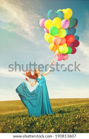 Luxury fashion stylish woman with balloons in hand on the field against the sky and  the sun in long dress