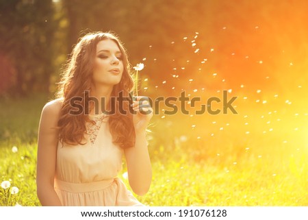 Beautiful young woman blowing dandelion. Trendy young girl at sunset with flower