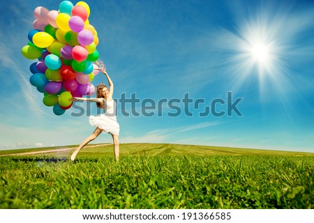 Happy birthday woman against the sky with rainbow-colored air balloons in hands. sunny and positive energy of nature. Young beautiful girl on the grass in the park.