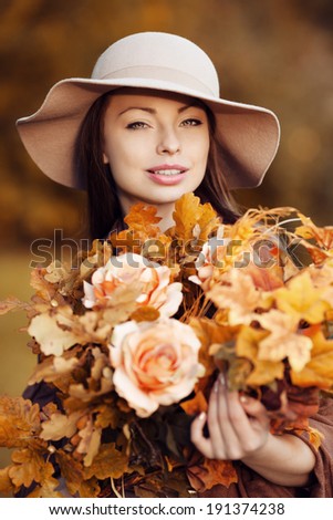 Young fashion woman  walking in autumn park with a bouquet of fall leaves of maple and oak autumn roses.