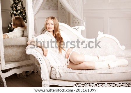 Beautiful young woman in white near the Christmas tree. Beautiful girl celebrates Christmas near the mirror