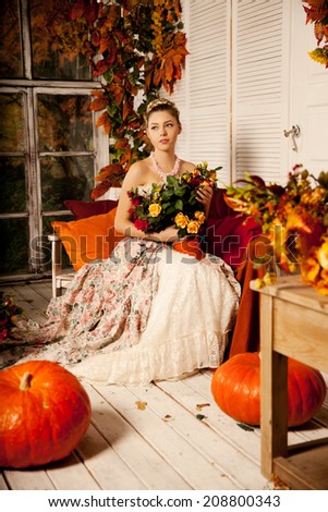 Young beautiful woman in vintage dress on autumn porch. Beauty girl in fall orange leaves
