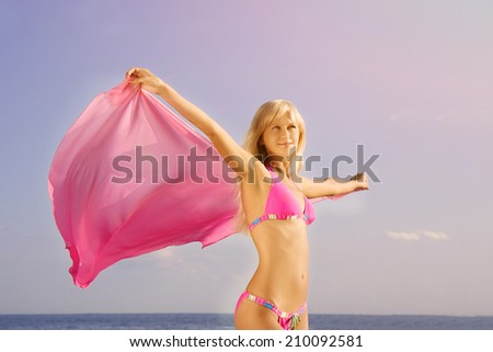 Young woman in bikini on beach with her his hands up. Girl with her arms up in the sea at sunset.